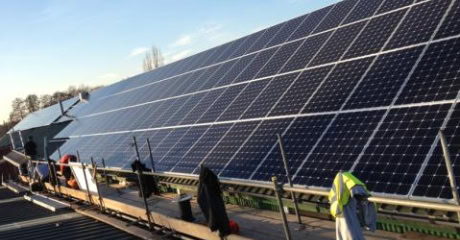 Installation of large commercial solar panels on a sloped rooftop, with workers ensuring optimal setup for renewable energy generation. ARC Renewables provides expert solar panel solutions for businesses across the UK.