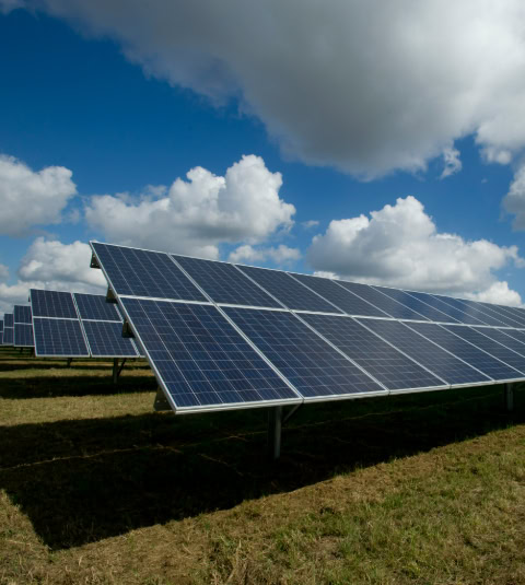 Ground-mounted solar panels in an open field generating renewable energy under a partly cloudy sky.